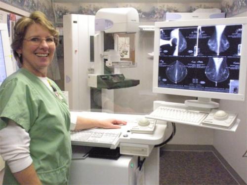 female nurse standing and smiling next to a mammogram machine